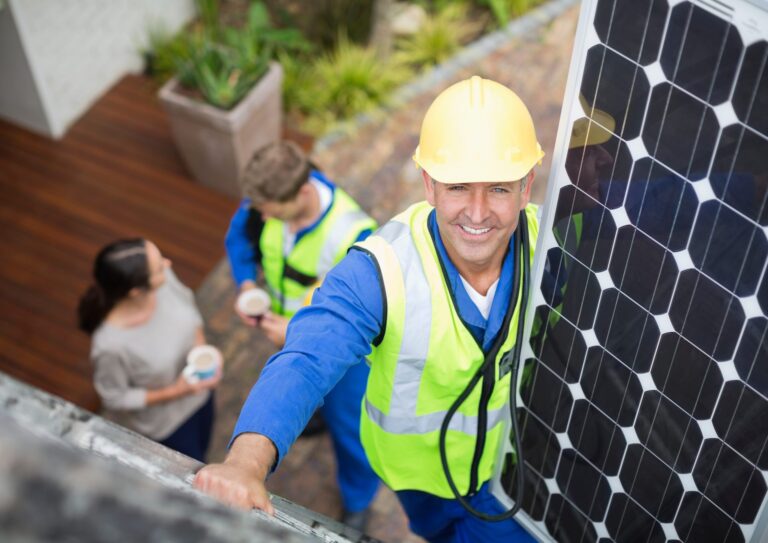 A friendly solar panel system installer is climbing onto the roof, carrying a panel and smiling at the camera. It's better not to diy solar.