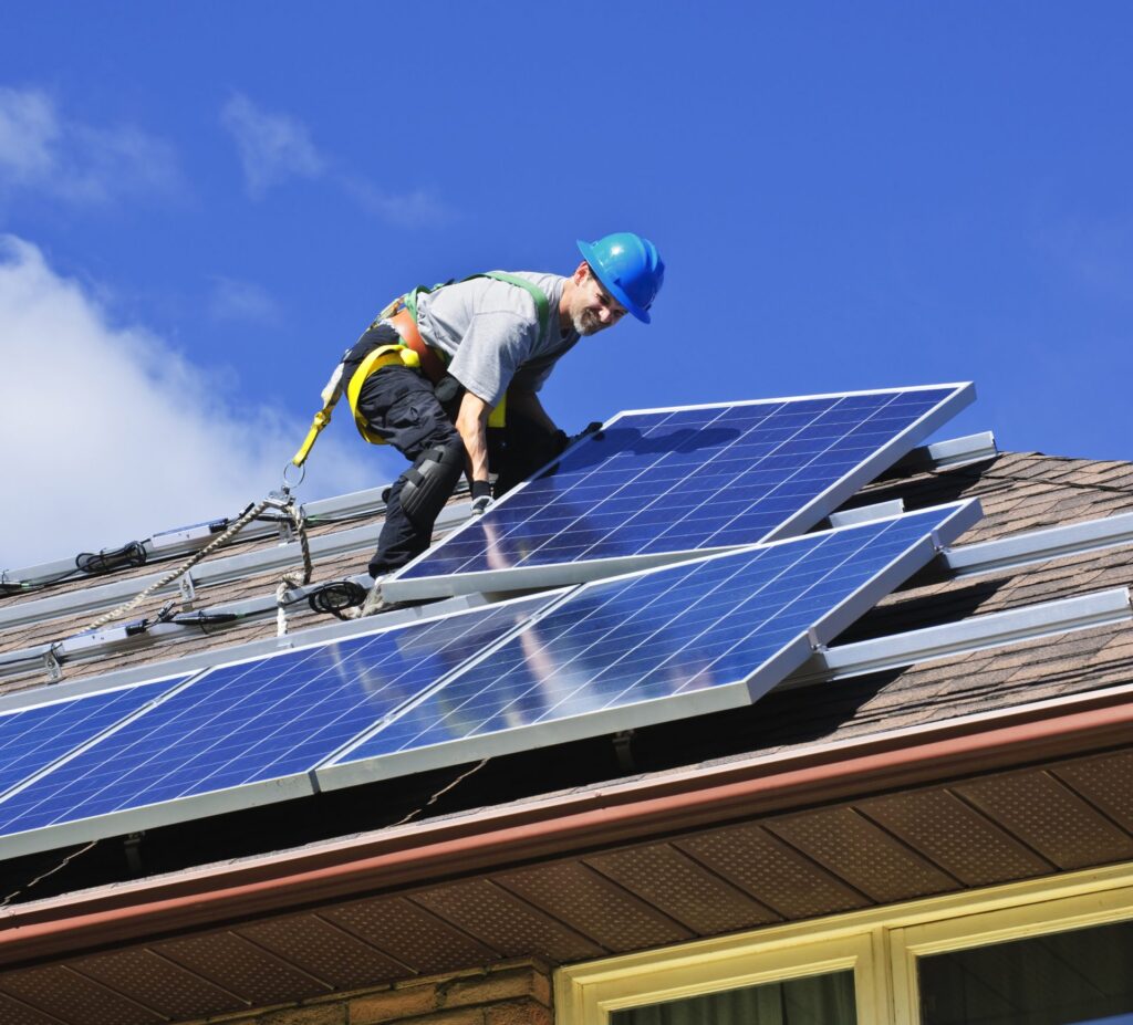 A worker standing on a roof installing solar power.